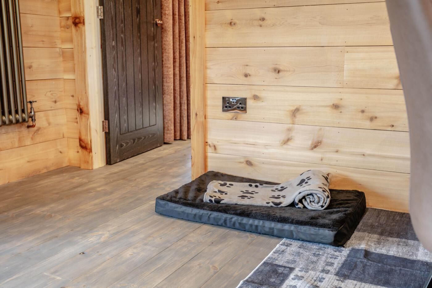Un intérieur en bois avec un panier pour animaux de compagnie, un radiateur et une porte.