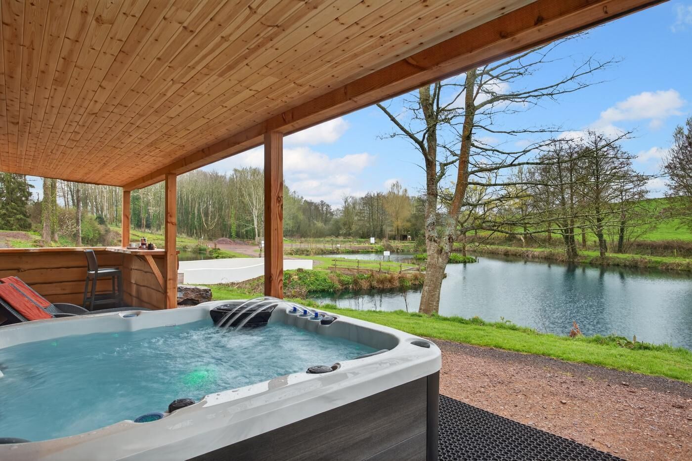 Un bain à remous avec une terrasse en bois et une vue sur un lac et des arbres.