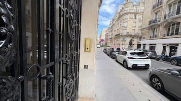 A street view with parked cars, a building with ornate black gates, and classic European architecture.