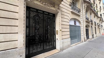 A building facade with ornate architectural details, a large black gate, and a street view.