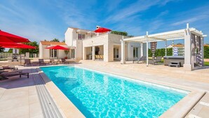 A swimming pool with lounge chairs and umbrellas, a covered seating area, and a building with a balcony. - Casa Andrik - Five Bedroom Villa, Sleeps 12 (Režanci)