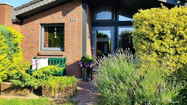 A brick building with a number '155' on the side, a green bench, and a planter with flowers. - Cozy studio vacation home in the Fedderwardersiel vacation park. Dogs allowed. (Butjadingen)
