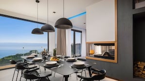 Un comedor moderno con vista panorámica al océano, chimenea y un ventanal grande.