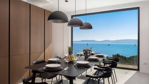 Un comedor moderno con una gran mesa dispuesta para seis personas, con vistas a un paisaje marino.