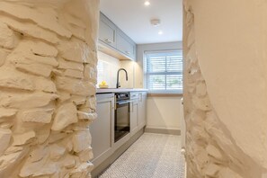 A narrow kitchen with white stone walls, a window with blinds, and a patterned floor. - 1 Bed in Ciliau Aeron (oc-b36926) (Ciliau Aeron)