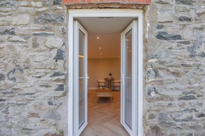A stone exterior wall with a door leading to an interior space with a wooden floor and a table with chairs. - 1 Bed in Ciliau Aeron (oc-b36926) (Ciliau Aeron)