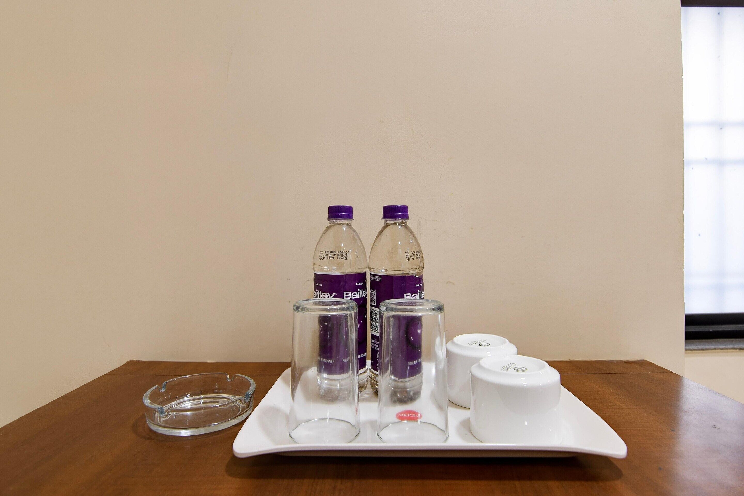 A tray with two bottles, a glass, and a white cup on a wooden table.