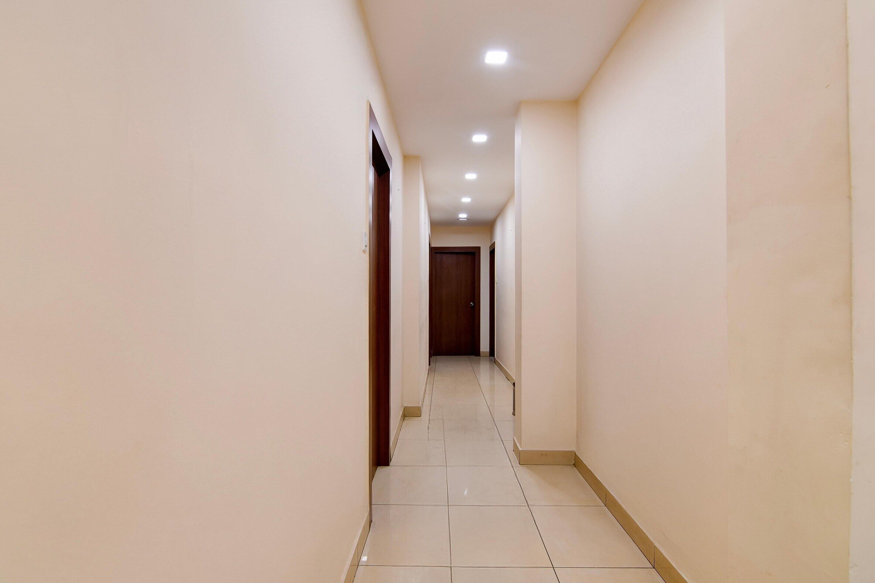 Un pasillo estrecho y bien iluminado, con piso de baldosas y una puerta de madera al final.