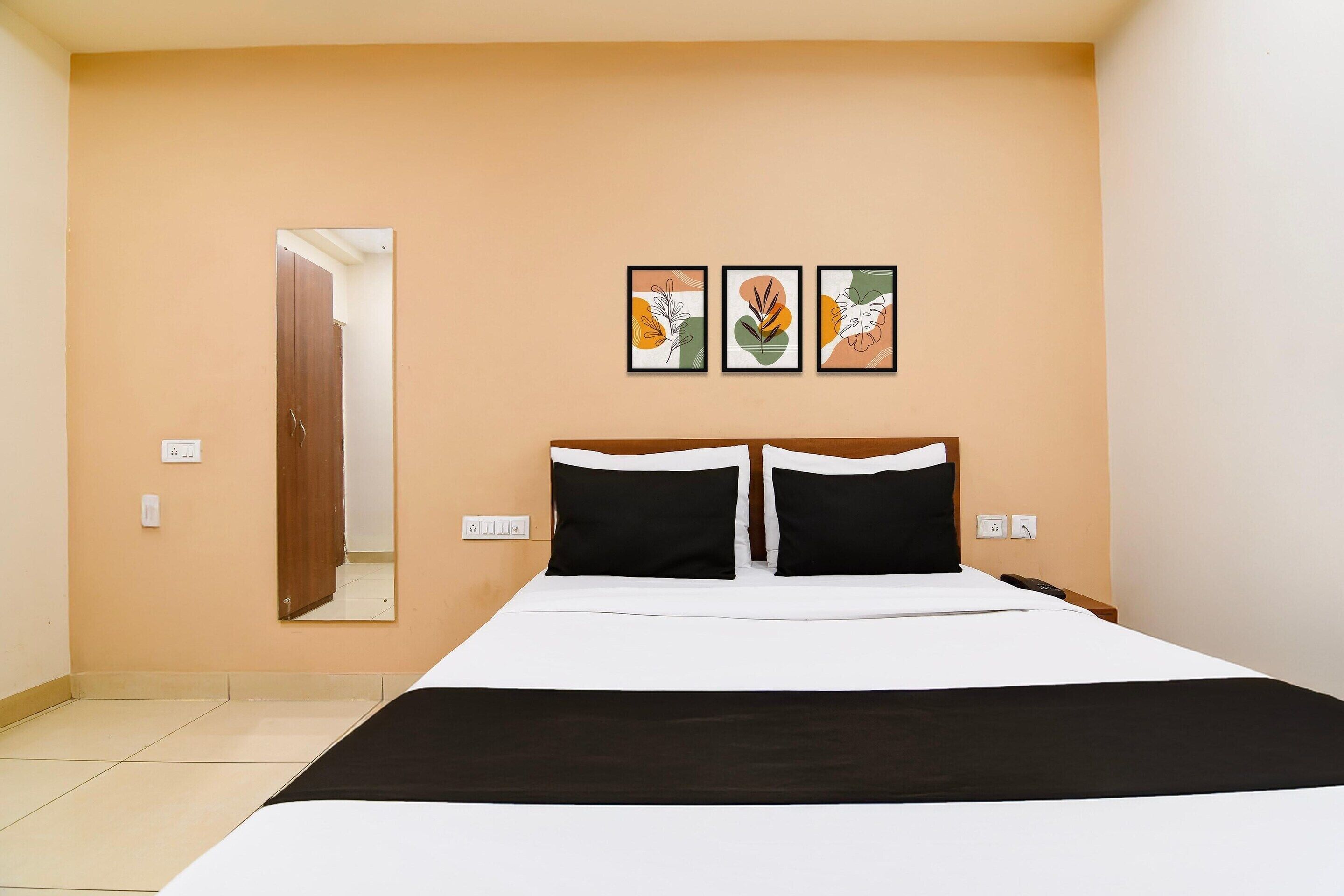 Een hotelkamer met een bed, een spiegel en drie kunstwerken in lijsten aan de muur.