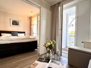 A hotel room with a bed, a glass table with a magazine, a vase with flowers, and a view of a balcony. - Hochwertige Ferienwohnung fur 3 im Seepark Sellin (Sellin)