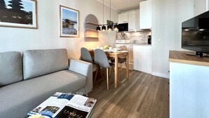 A modern apartment with a sofa, dining table, chairs, kitchen area, and a TV. - Hochwertige Ferienwohnung fur 3 im Seepark Sellin (Sellin)