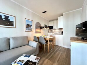 A modern apartment with a sofa, dining table, chairs, kitchen area, and a TV. - Hochwertige Ferienwohnung fur 3 im Seepark Sellin (Sellin)