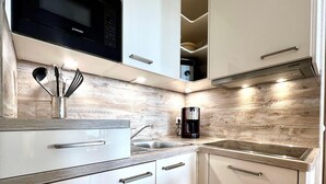 A modern kitchen with white cabinetry, a stainless steel sink, a black coffee maker, and a microwave above the counter. - Hochwertige Ferienwohnung fur 3 im Seepark Sellin (Sellin)