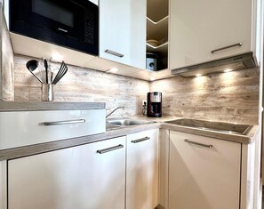 A modern kitchen with white cabinetry, a stainless steel sink, a black coffee maker, and a microwave above the counter. - Hochwertige Ferienwohnung fur 3 im Seepark Sellin (Sellin)