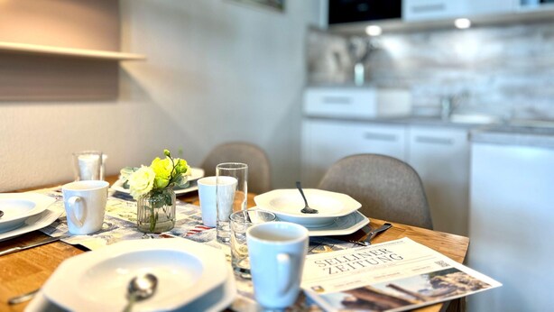 A dining area with a table set for two, a vase with flowers, and a magazine on the table. - Hochwertige Ferienwohnung fur 3 im Seepark Sellin (Sellin)