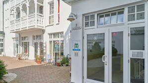A building with a white facade, a balcony with white railings, a glass door entrance, and a sign indicating a restaurant. - Hochwertige Ferienwohnung fur 3 im Seepark Sellin (Sellin)