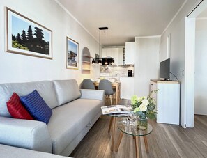 A modern living room with a sofa, dining table, and kitchen area in the background. - Hochwertige Ferienwohnung fur 3 im Seepark Sellin (Sellin)