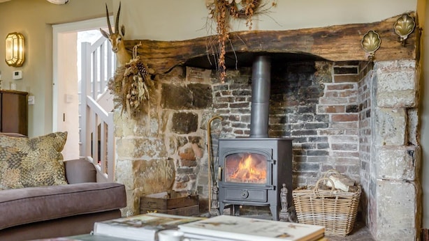 Ein gemütliches Wohnzimmer mit Kamin aus Stein, einer Couch und einem Tisch mit Büchern und Teetassen.
