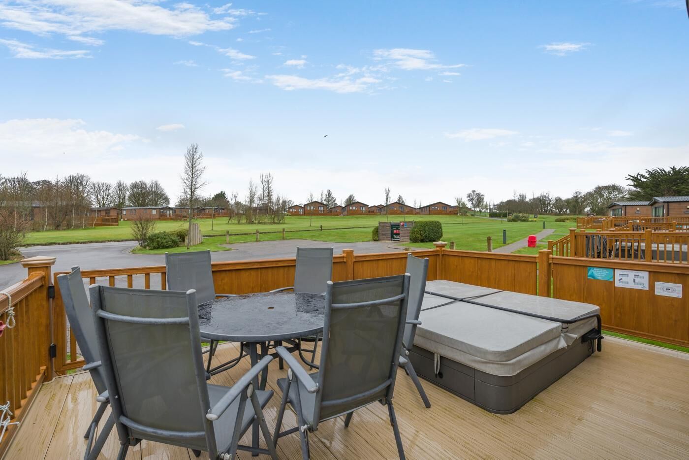 A deck with a table and chairs, overlooking a grassy area with buildings in the background.