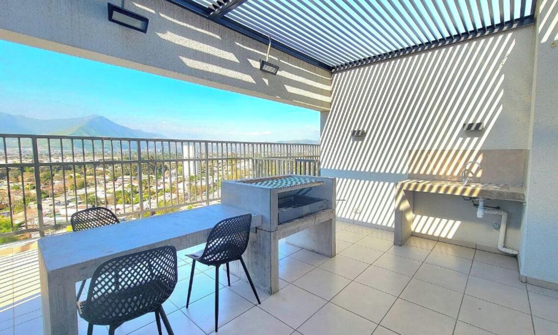 A balcony with a grill, chairs, and a view of a mountainous landscape.