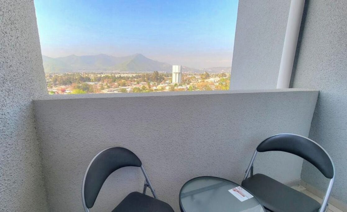 Varanda com duas cadeiras e uma mesa, com vista para um horizonte urbano e montanhas ao longe.