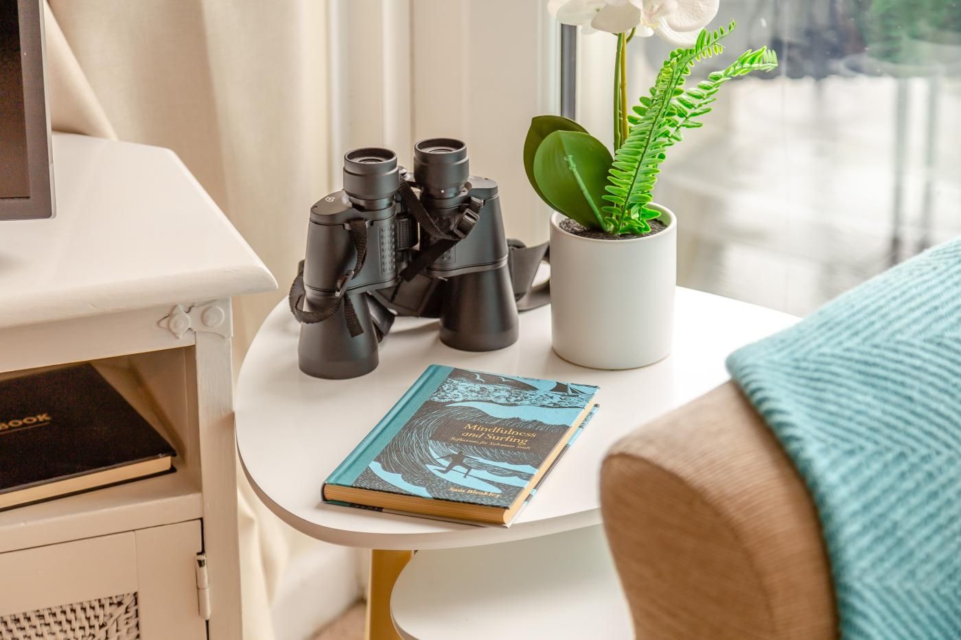 A white table with a book titled 'Mindfulness and Surfing' and a pair of binoculars.