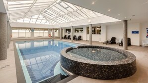 Une piscine intérieure dotée d’un toit en verre, d’un jacuzzi et d’espaces aménagés pour se détendre.