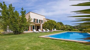 Una casa de dos pisos amb piscina, gespa verda i gandules.