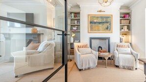 Un salon moderne avec deux fauteuils blancs, une cheminée, une bibliothèque et un grand tableau abstrait.