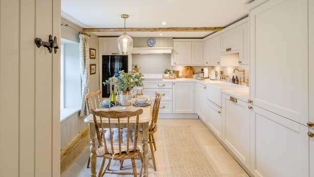 A kitchen with white cabinets, a wooden dining table with chairs, a hanging light fixture, and a window with curtains. - 2 Bed in Glenshee (oc-l37493) (Spittal of Glenshee)