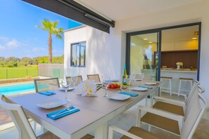 A dining area with a pool view, a kitchen, and a palm tree outside. - Villa Pleta - Four Bedroom Villa, Sleeps 8 (Mallorca)