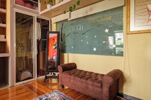 Una habitación con puerta de vidrio corrediza que da a un armario, un sofá marrón con capitoné, una alfombra colorida y una pared con un letrero que dice 'LAUGH' y elementos decorativos.