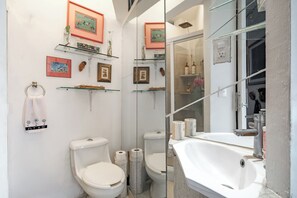 Un baño con dos inodoros, cabina de ducha con mampara de vidrio, lavamanos y fotografías enmarcadas en la pared.