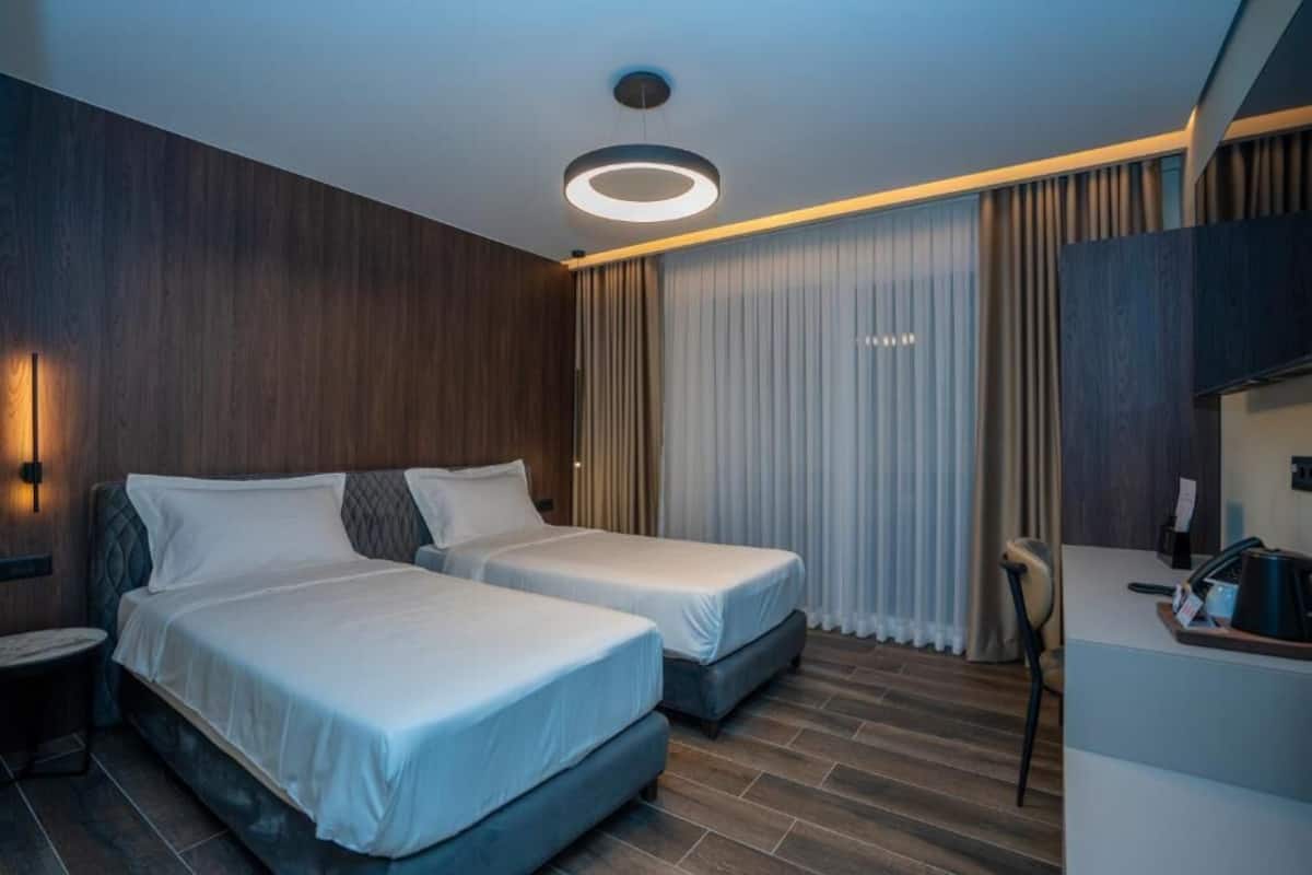 Ett hotellrum med två sängar, ett skrivbord, en stol och en modern taklampa.