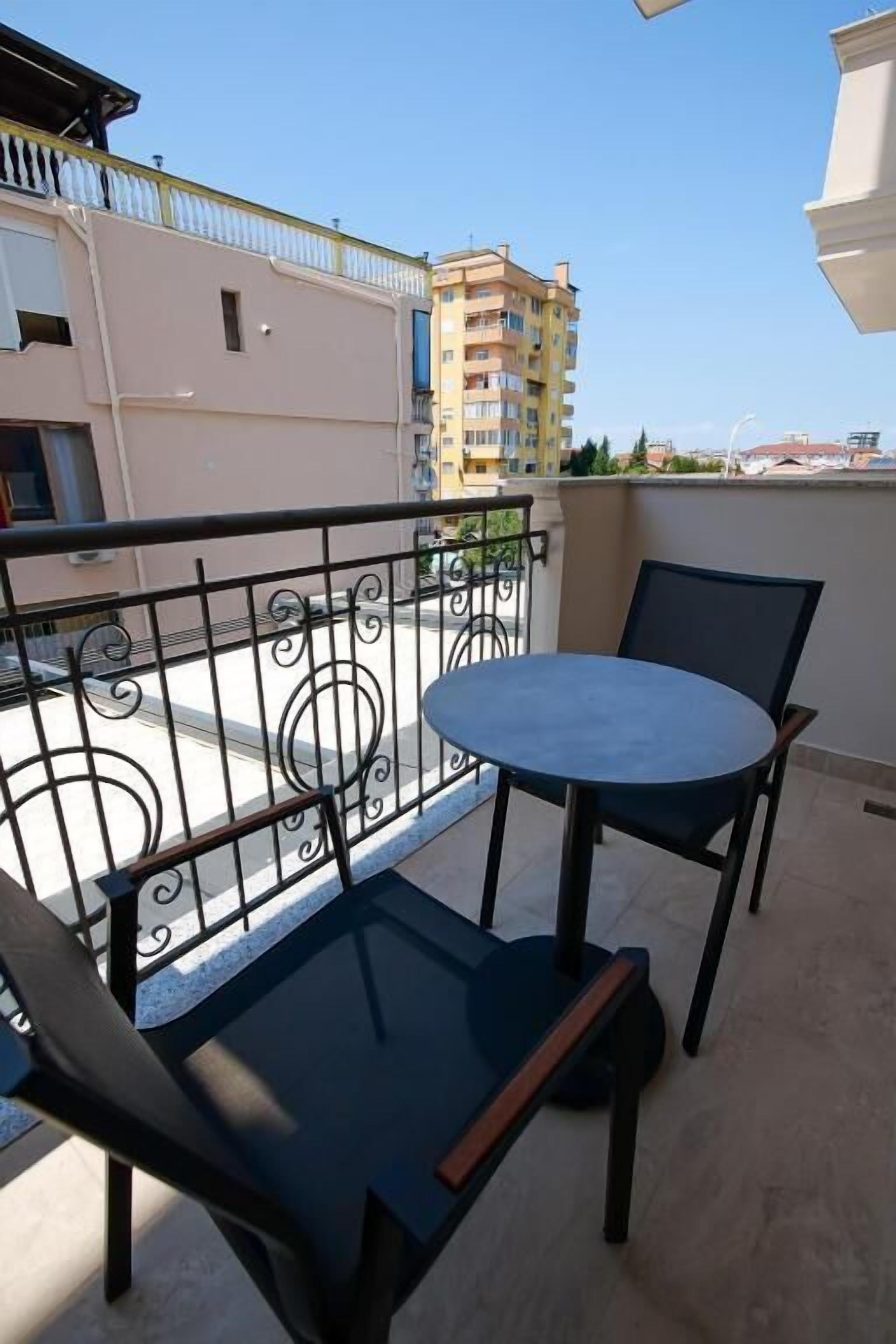 A balcony with a round table and two chairs, a metal railing, and buildings in the background.