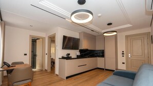 Uma sala moderna com sofá, uma mesa de jantar com cadeiras, uma cozinha com bancada e armários, e um corredor que leva a outro cômodo.