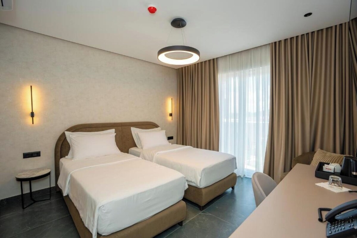 A hotel room with two beds, a desk, a chair, a telephone, and a window with curtains.