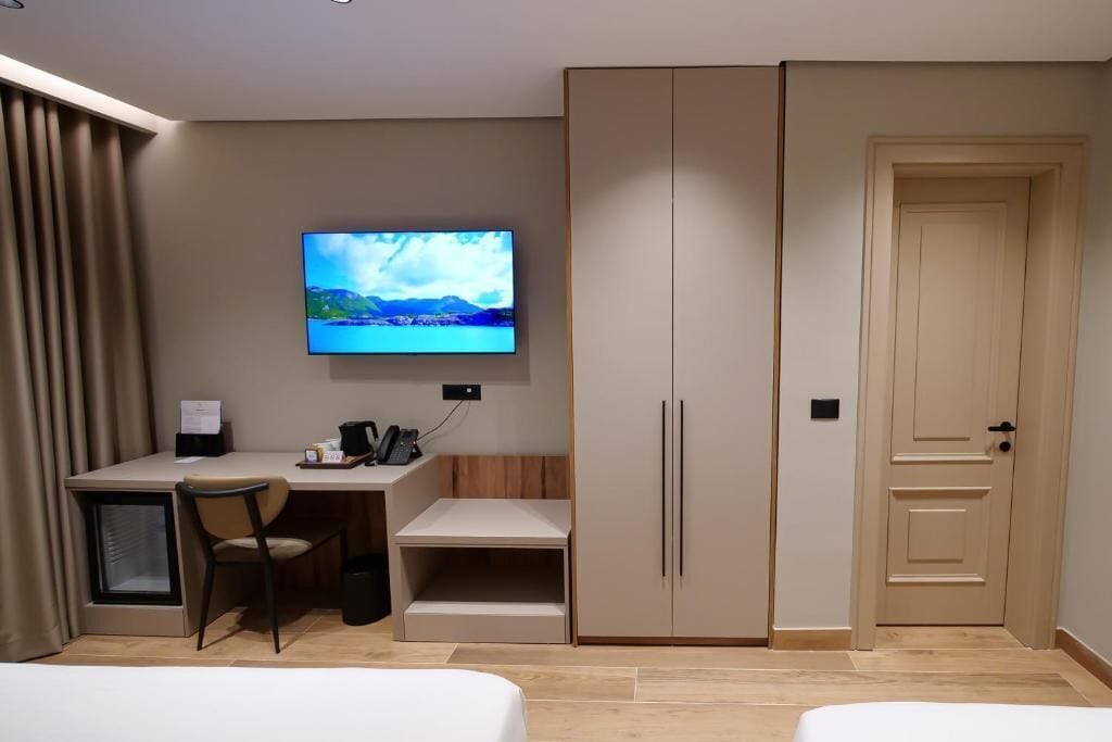 Quarto de hotel com cama, secretária com cadeira, televisão e armário.