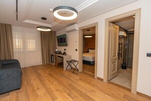 Quarto de hotel moderno com piso de madeira, uma escrivaninha, cama e área de chuveiro.