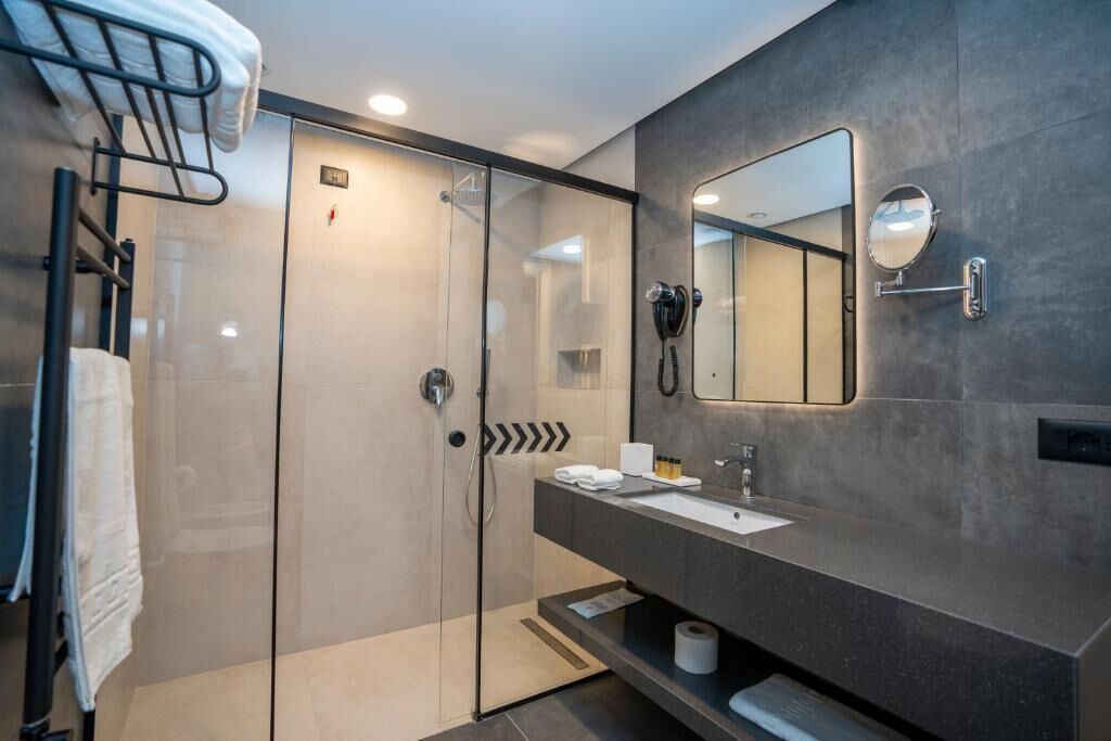 Un baño moderno con ducha acristalada, tocador con espejo y un perchero para toallas.
