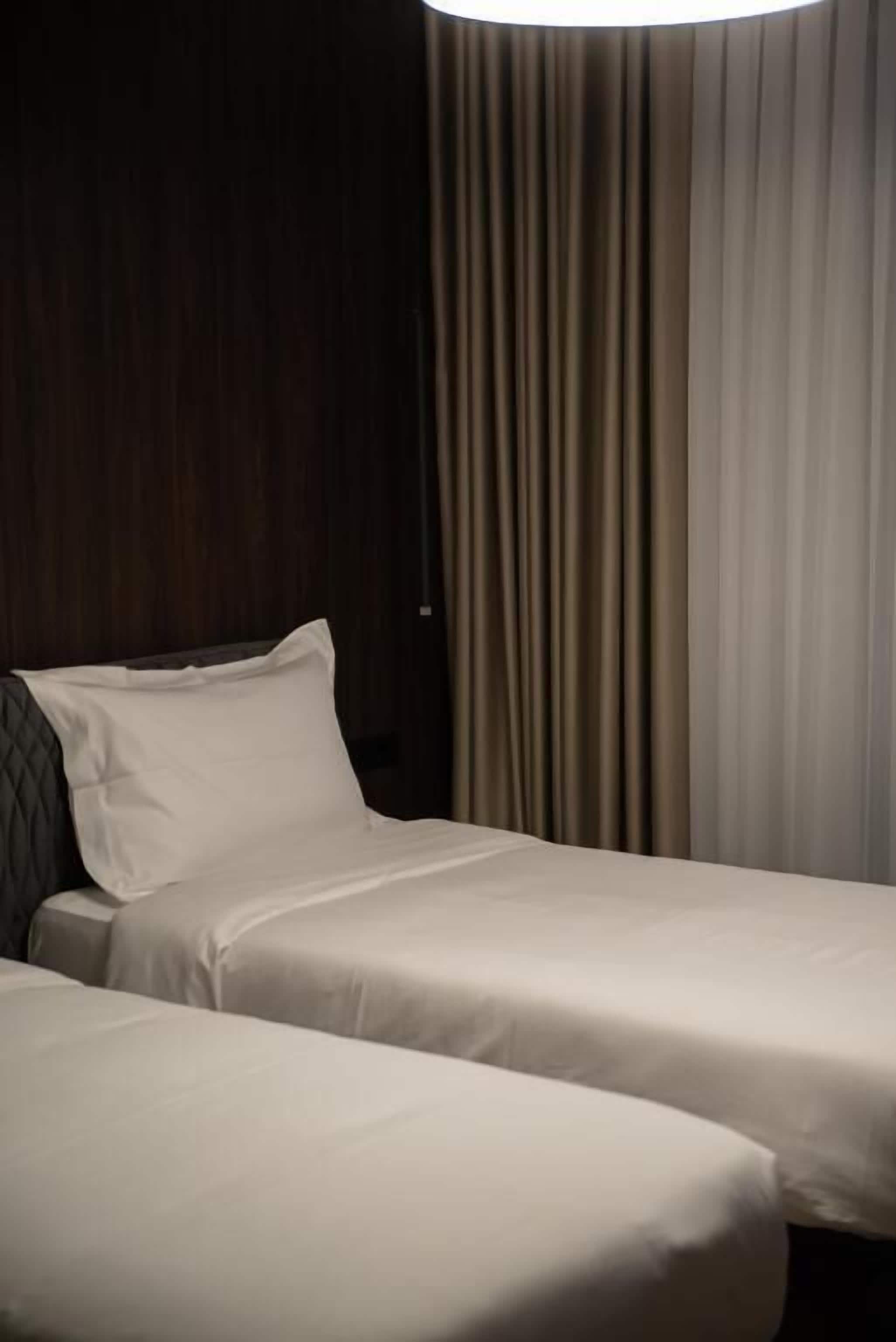 A hotel room with two beds, a dark wooden headboard, and a curtain.
