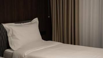 Quarto de hotel com duas camas, cabeceira de madeira escura e cortina.