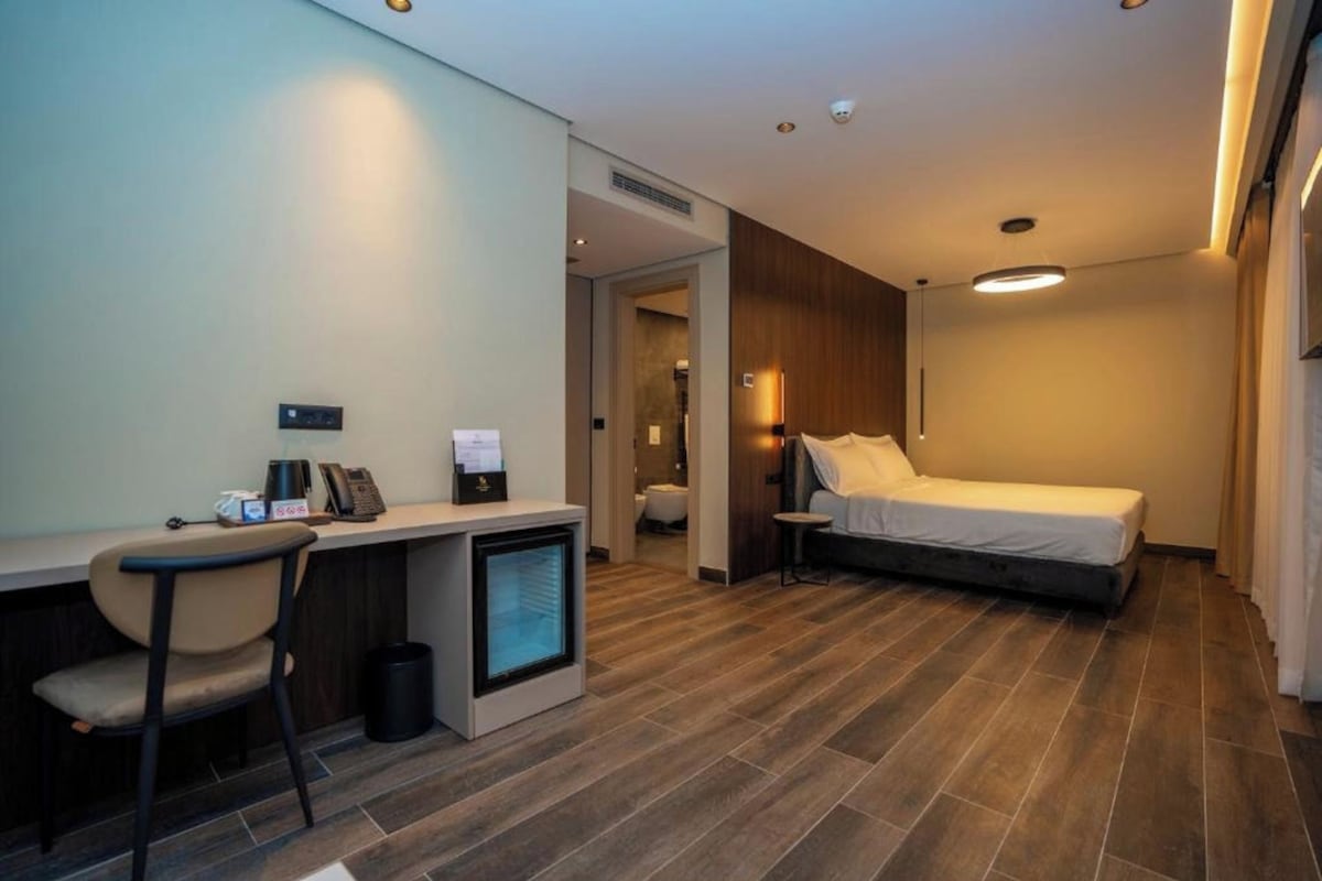 A hotel room with a bed, a desk, a chair, a small TV, and a bathroom visible through an open door.