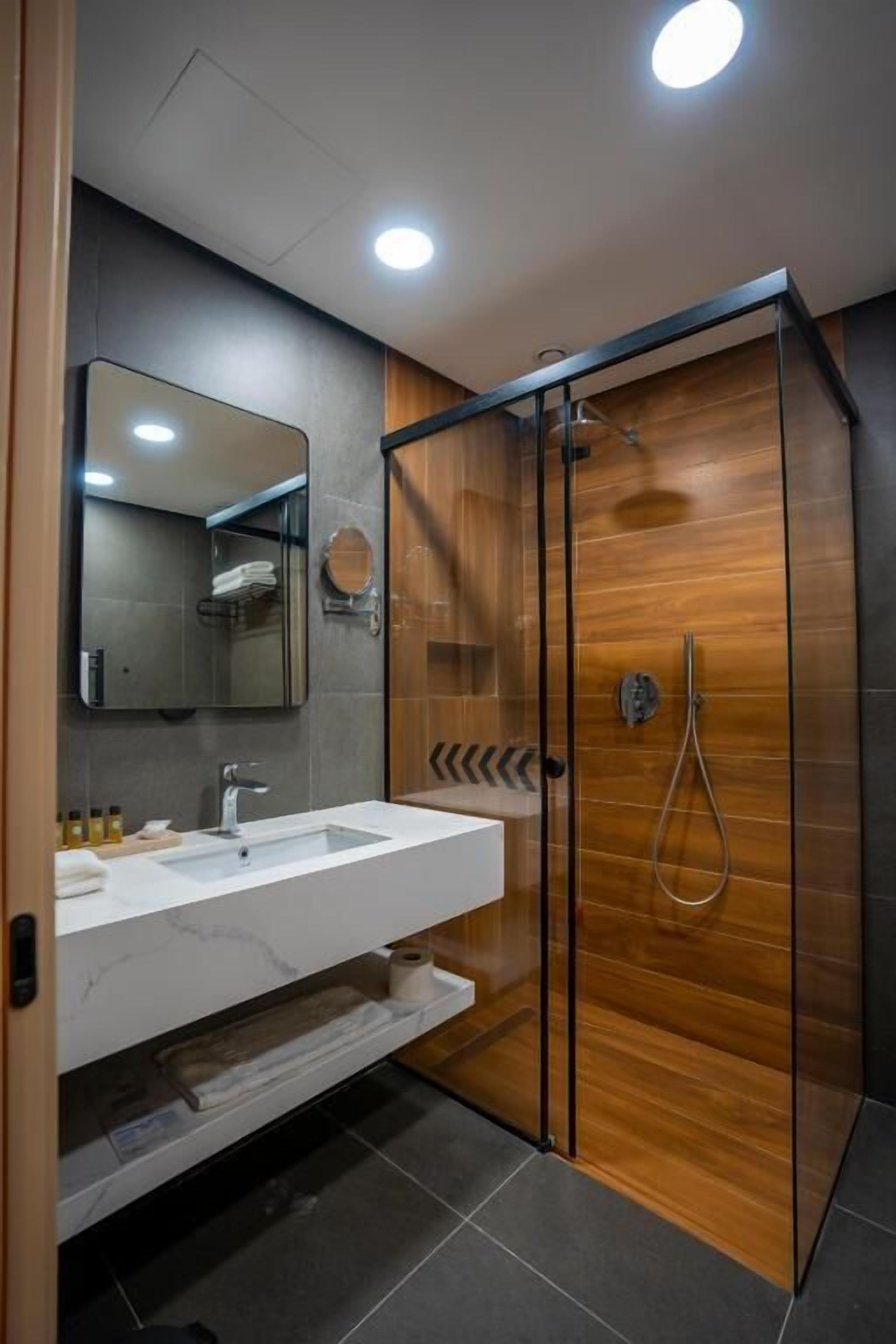 Un baño moderno con cabina de ducha de vidrio, un lavabo blanco y un espejo.
