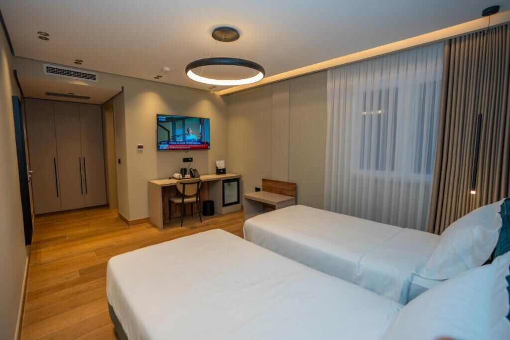 Une chambre d’hôtel avec deux lits, un bureau, une télévision et une grande fenêtre avec des rideaux.