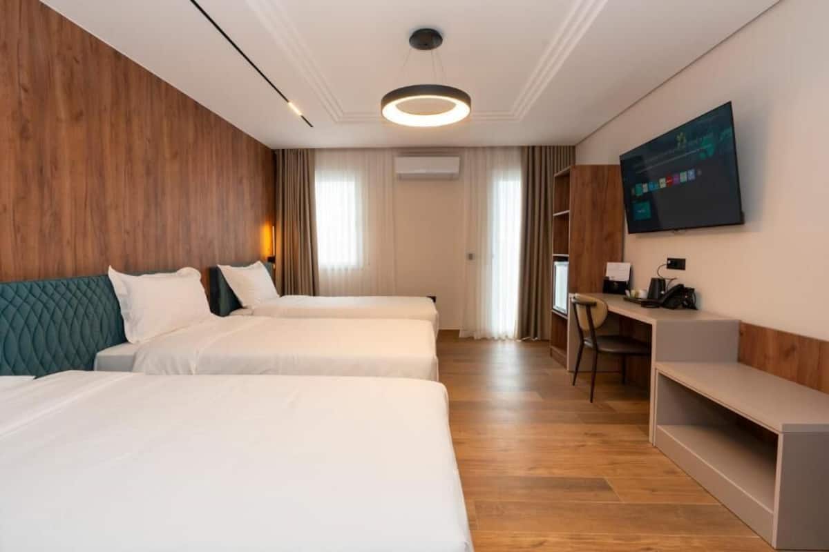 Ett hotellrum med två sängar, ett skrivbord, en stol, en tv och en väggpanel av trä.