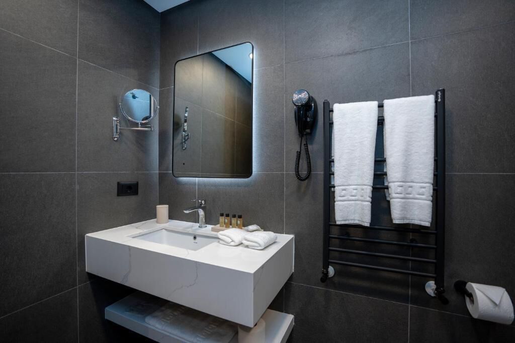A modern bathroom with a large mirror, a sink, a hairdryer, and a towel rack.