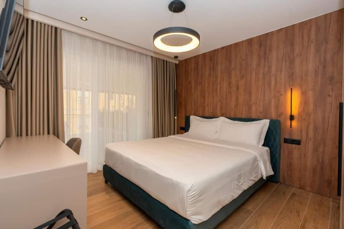 Ett modernt hotellrum med en säng, ett skrivbord och ett stort fönster med gardiner.