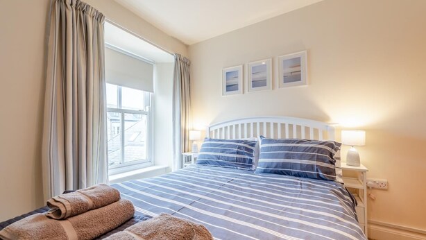 Ein Hotelzimmer mit Bett, zwei Nachttischlampen, einem Fenster mit Vorhängen und drei gerahmten Bildern an der Wand.