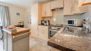 Eine moderne Küche mit hellen Holzschränken, einer Granit Arbeitsplatte, einem Einbauofen, einer Mikrowelle und einem Spülbecken.
